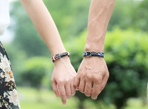 Close-up of couple holding hands wearing woven leather guitar charm bracelets in nature