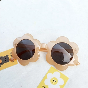 Nude pink flower shaped kids sunglasses with dark round lenses on a white textured cloth