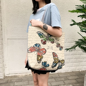 Artistic canvas tote bag with butterfly print and vintage handwriting shown outdoors