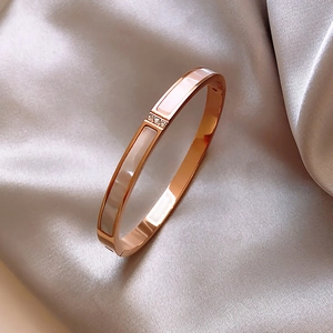 Detail of rose gold stainless steel bangle with shell inlay and diamonds on silk