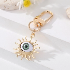 Golden sun-shaped keychain with a green evil eye crystal charm on a white texture