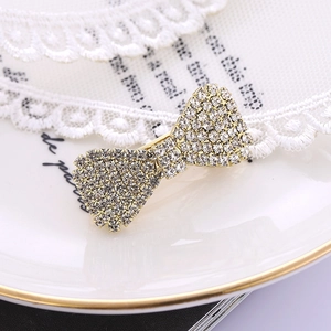 Elegant gold bow hair clip with sparkling rhinestones on white lace and ceramic tray