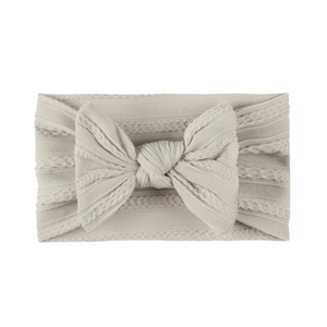 Detail of beige jacquard nylon baby headband featuring cable knit texture and large bow