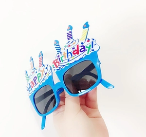 Close-up of blue Happy Birthday party glasses with candle toppers held against white background