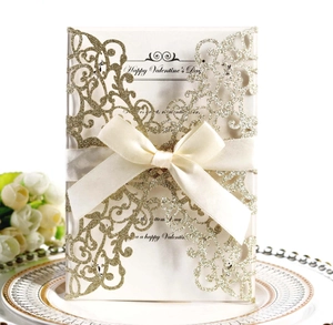Detail of gold glitter laser-cut wedding invitation with beige ribbon bow and pearl paper