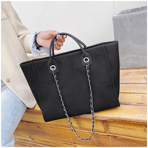 Detail of black large-capacity tote bag with silver chain strap on wooden steps
