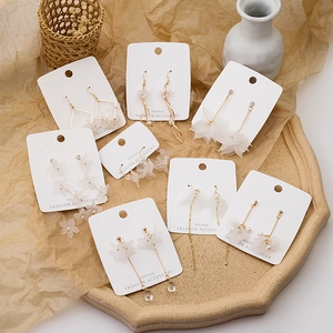 Detailed display of white floral and tassel earrings on a ceramic tray with dry flowers
