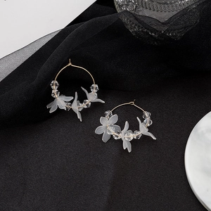 Detail of white matte flower earrings with clear beads and gold hooks on dark surface