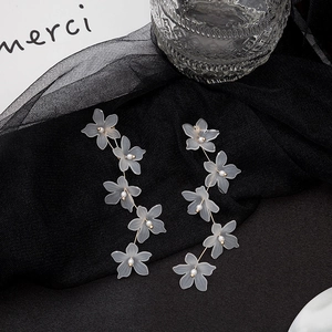 Elegant long white flower drop earrings with pearls on a textured black mesh background