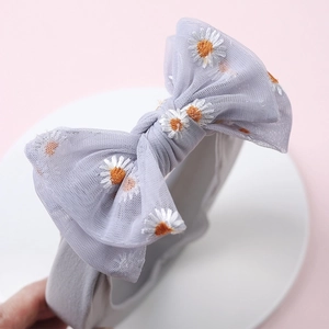 Detail of grey tulle baby headband featuring embroidered daisy flowers and a large bow