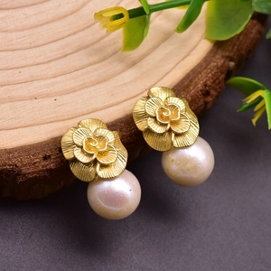 Macro detail of vintage champagne gold floral earrings with natural pearls on wood
