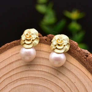 Detailed macro shot of golden rose earrings with Edison pearls on a rustic wood base
