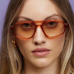 Close-up of orange aviator sunglasses with transparent frames on female model face
