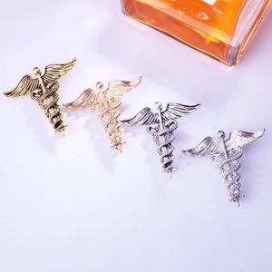 Close-up detail of retro winged snake caduceus metal brooch pin in four metallic finishes.