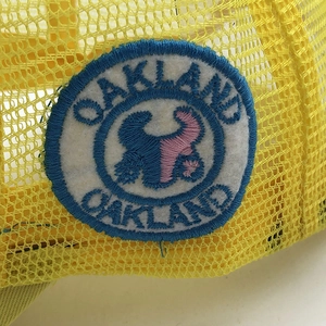 Detailed close-up of yellow trucker hat with embroidered blue Oakland text and mesh texture
