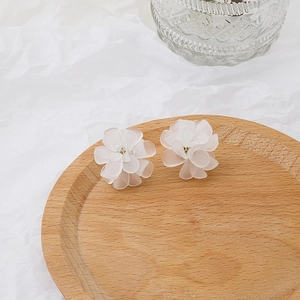 Macro shot of white matte flower earrings with gold center on a round wooden tray