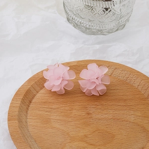 Close-up of pink floral stud earrings on a wooden tray with a white aesthetic background