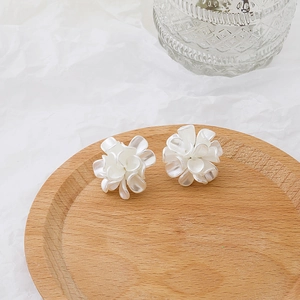 Detailed view of 3D white flower earrings featuring layered petals on a wooden tray