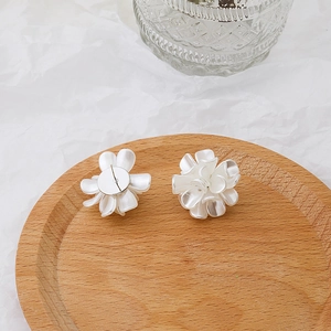 Detailed view of matte white 3D flower stud earrings placed on a natural wood tray
