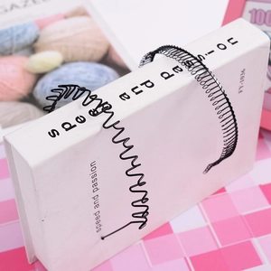 Gros plan d'un serre-tête métallique noir ondulé sur un livre avec fond à motifs roses