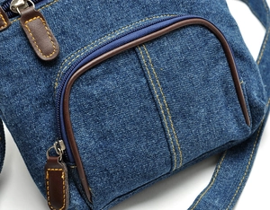 Detailed close-up of blue denim crossbody bag with yellow stitching and brown leather trim