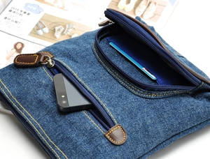 Detail of blue denim shoulder bag featuring dual front zipper pockets and leather pulls