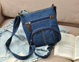 Classic blue denim crossbody bag with brown leather trim styled on a beige sofa