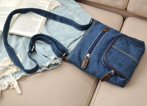 Close-up of blue denim crossbody bag featuring front zipper pocket with brown leather pull