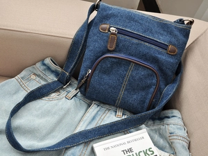 Detail of blue denim crossbody bag with brown leather zipper pulls on denim jeans