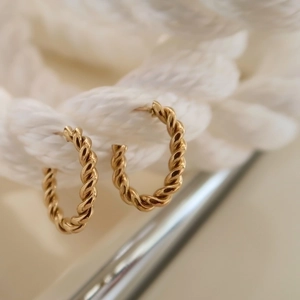 Macro shot of gold C-shaped twisted hoop earrings hanging on a white textured rope