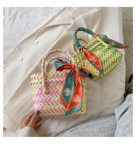 Detail of woven straw handbag featuring contrast colors and a decorative Peace silk scarf
