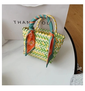 Detail of woven straw handbag with colorful patterns and silk scarf handle on table