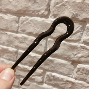 Detail of a dark brown wavy U-shaped resin hair fork held in hand for bridal styling