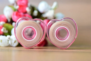 Detailed view of two nude eyelid tapes stored in heart-shaped pink transparent cases