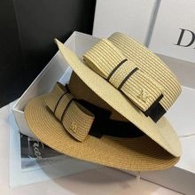 Detail of flat top straw boater hats featuring black grosgrain ribbons and gold M logos