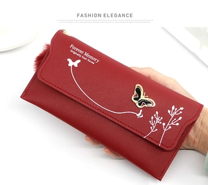 Detail of red long wallet with butterfly pattern, textured leather and fur ball charm