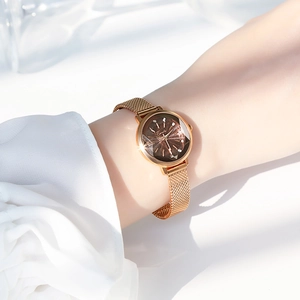 Detail of rose gold mesh strap watch with brown dial worn on female wrist in soft light