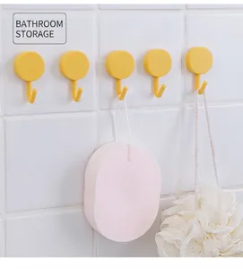 Row of five yellow rotating bathroom hooks mounted on white tiles with shower sponges