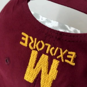 Gros plan détaillé de la broderie jaune EXPLORE et W sur la casquette en coton bordeaux