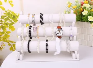 Three-tier white velvet jewelry stand displaying bracelets and watches in home setting