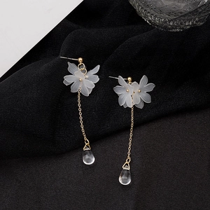 Detailed close-up of long gold chain earrings with white matte petals and clear teardrop