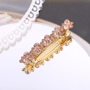 Detail of a golden metal hair clip with pink faceted rhinestones on a mirror surface