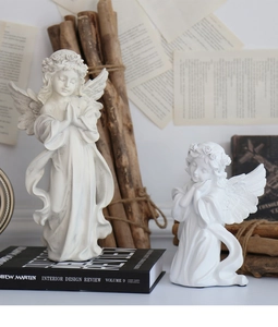 Close-up of ivory resin angel statues with prayer poses on vintage books