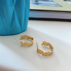 Detailed view of gold C-shaped earrings with irregular hammered texture on a blue background