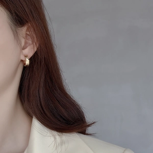 Macro shot of minimalist gold hoop earrings with textured hammered finish on a model