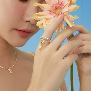 Golden layered ring with tassel charm and crystals shown on hand with a flower