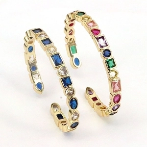 Bohemian C-shaped gold hoop earrings with multi-colored mixed-cut gemstones on white background