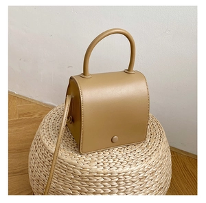 Minimalist khaki PU leather square bag displayed on a woven mat in an indoor setting