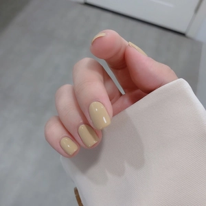 Glossy mustard yellow press-on nails shown on hand with neutral fabric background