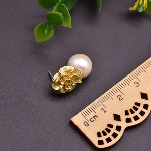 Close-up of golden flower stud earring with natural pearl next to a measuring ruler